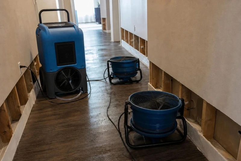Air movers and a dehumidifier drying a Little Elm hallway with the baseboard opened to the studs.